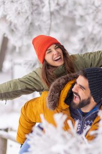 Boyfriend piggybacking girlfriend on snowy winter day Couple having fun on winter vacation, boyfriend piggybacking girlfriend while spending time outdoor on snowy winter day in mountains